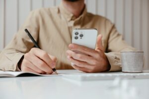 man writing and holding mobile phone